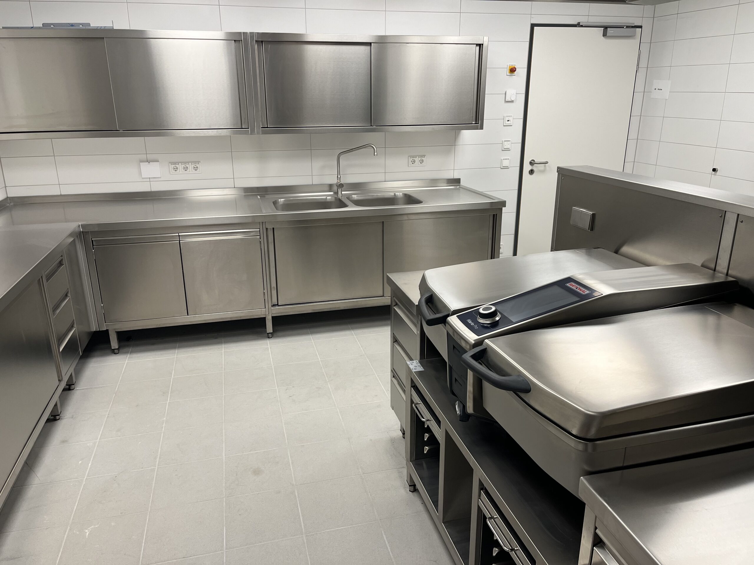 Edelstahl-Gewerbeküche mit einem Multifunktionskocher, Spülbecken, viel Arbeitsfläche und Stauraum – Referenz von Heiser's Küchen.